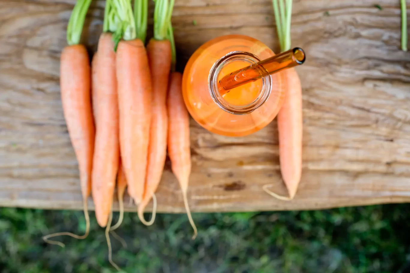 carrots on a bench with glass bottle with carrot juice inside and glass straw