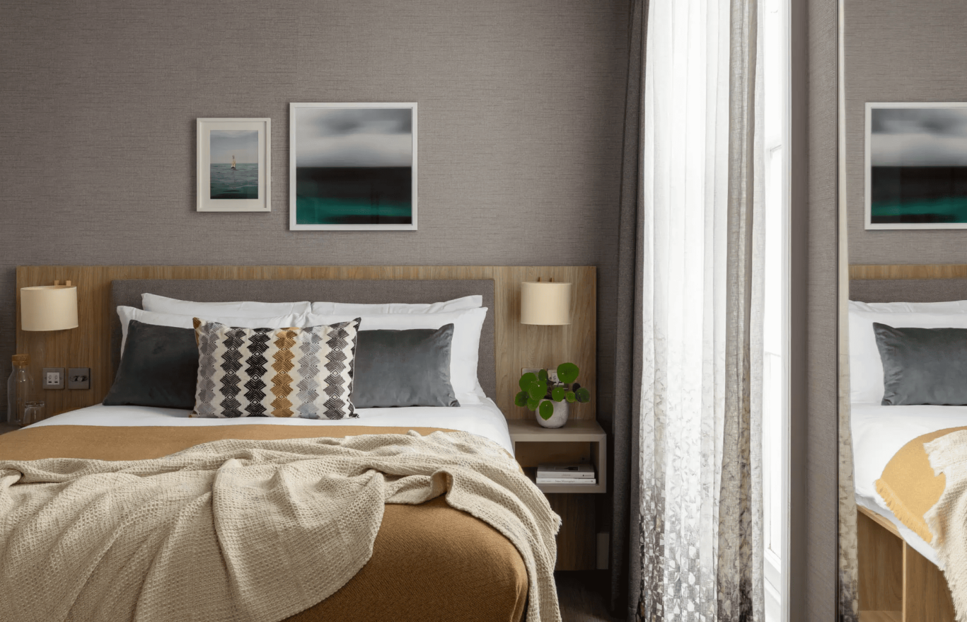 hotel bedroom with dark yellow and grey cushions and blankets
