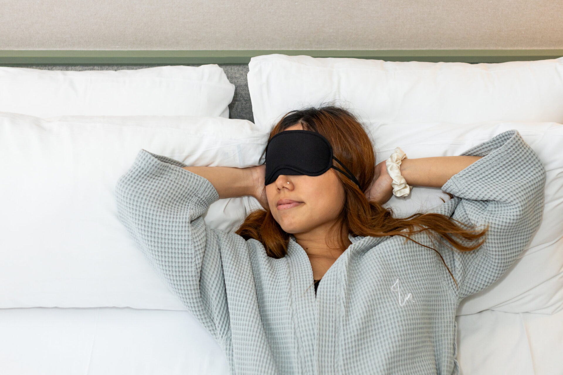 Woman in dressing gown and eye mask smiling while relaxing on a comfy double bed at Inhabit Hotels, Paddington and Bayswater.
